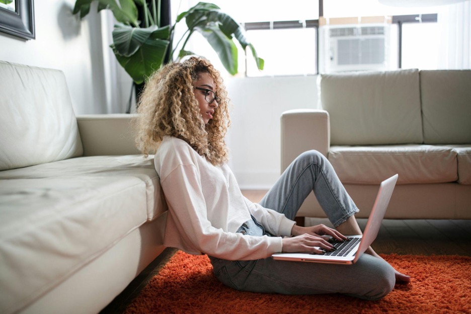 Woman sitting on a rug typing on a laptop that’s in her lap